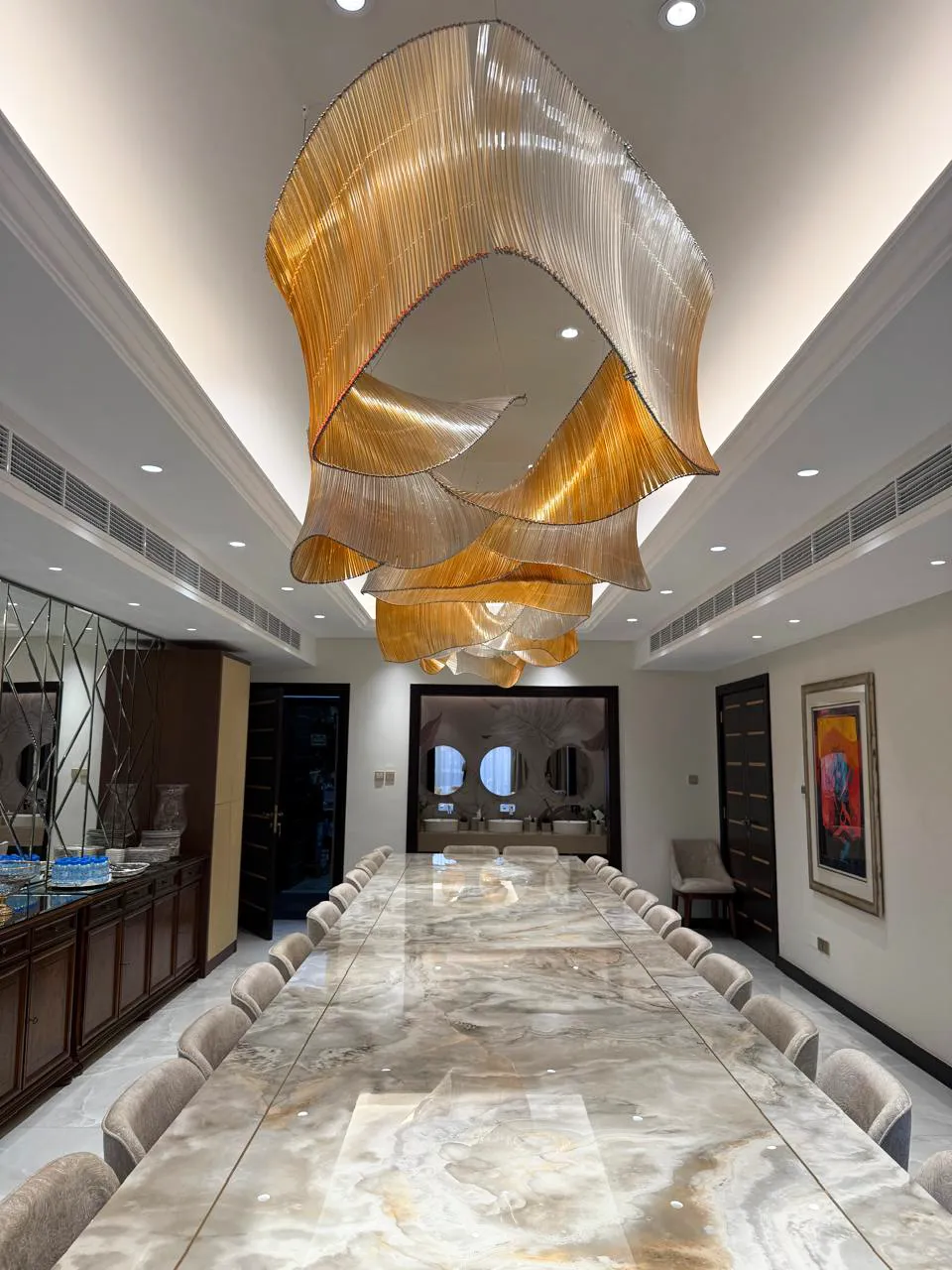 Grand renovated dining room with long stone table, beige upholstered chairs, dark wood doors