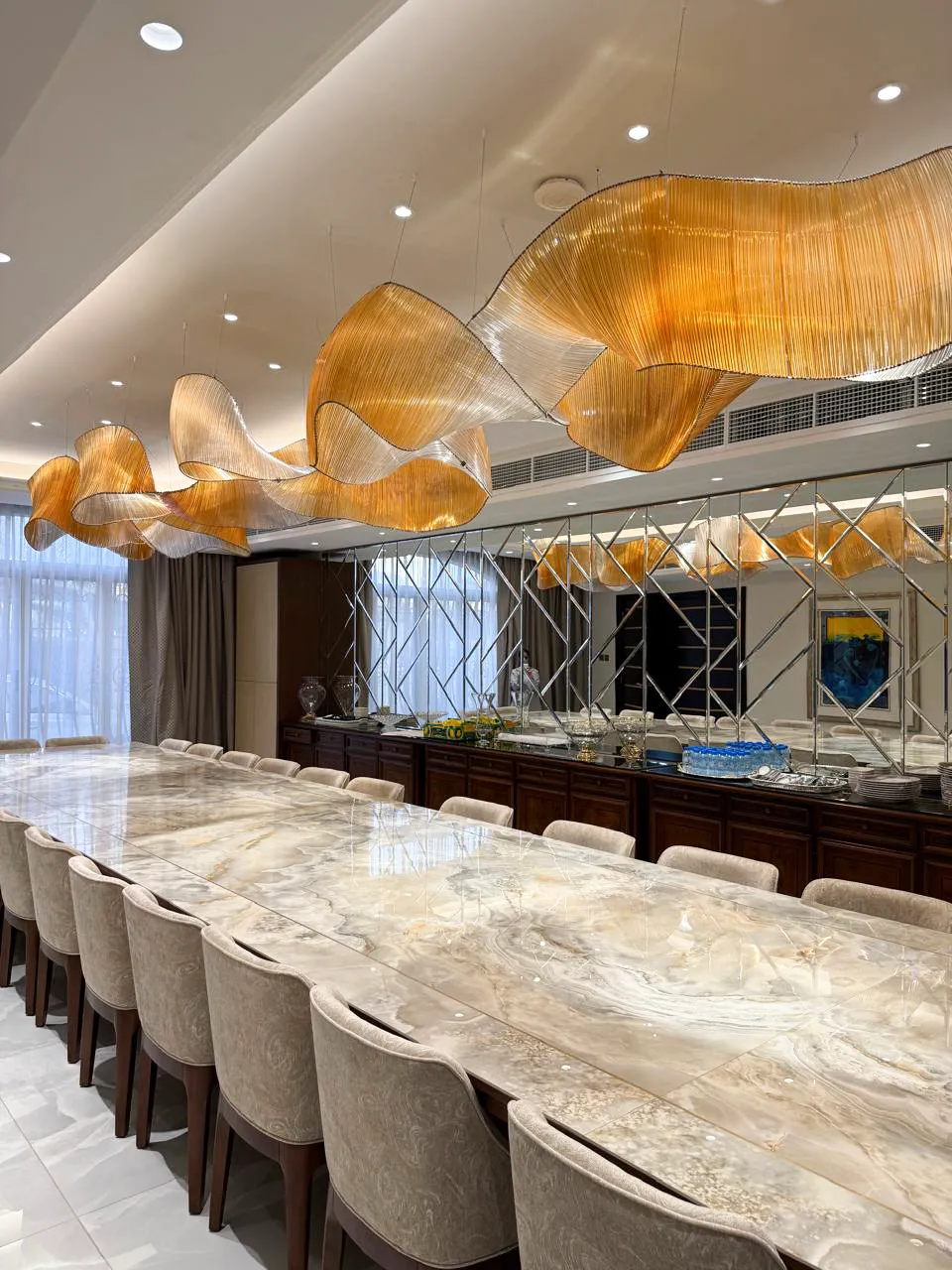 Long formal dining room after renovation with stone dining table, upholstered chairs, mirrored feature wall