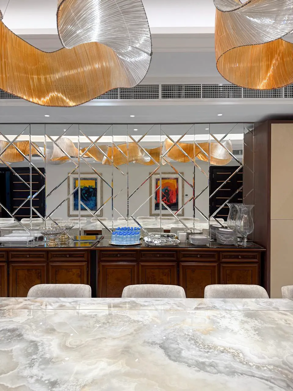 Luxury formal dining room design with marble-look stone table, mirrored wall, dark wood sideboard