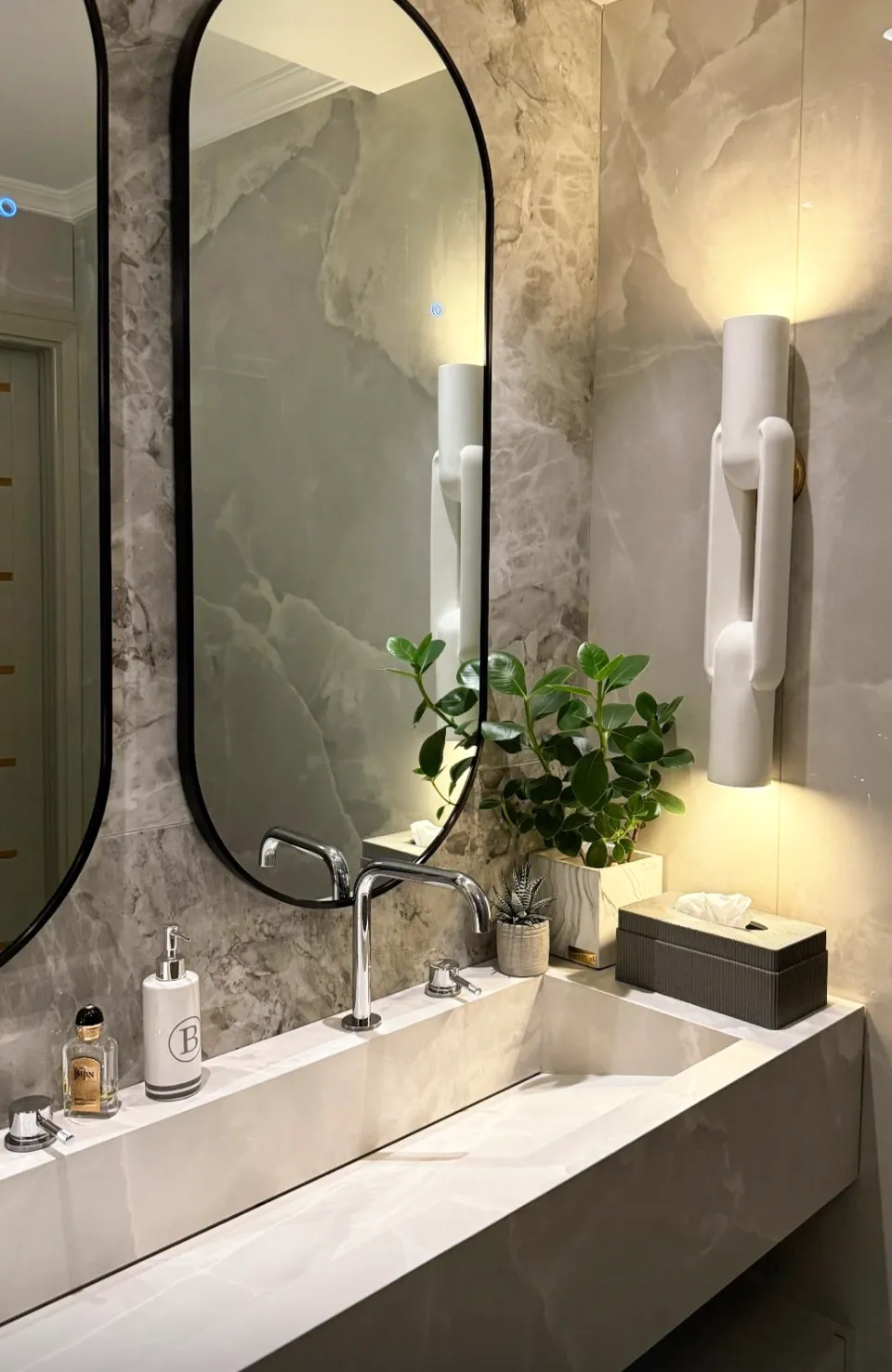 Powder room with arched black-framed mirrors, stone walls, integrated basin, plants, and modern white wall sconces