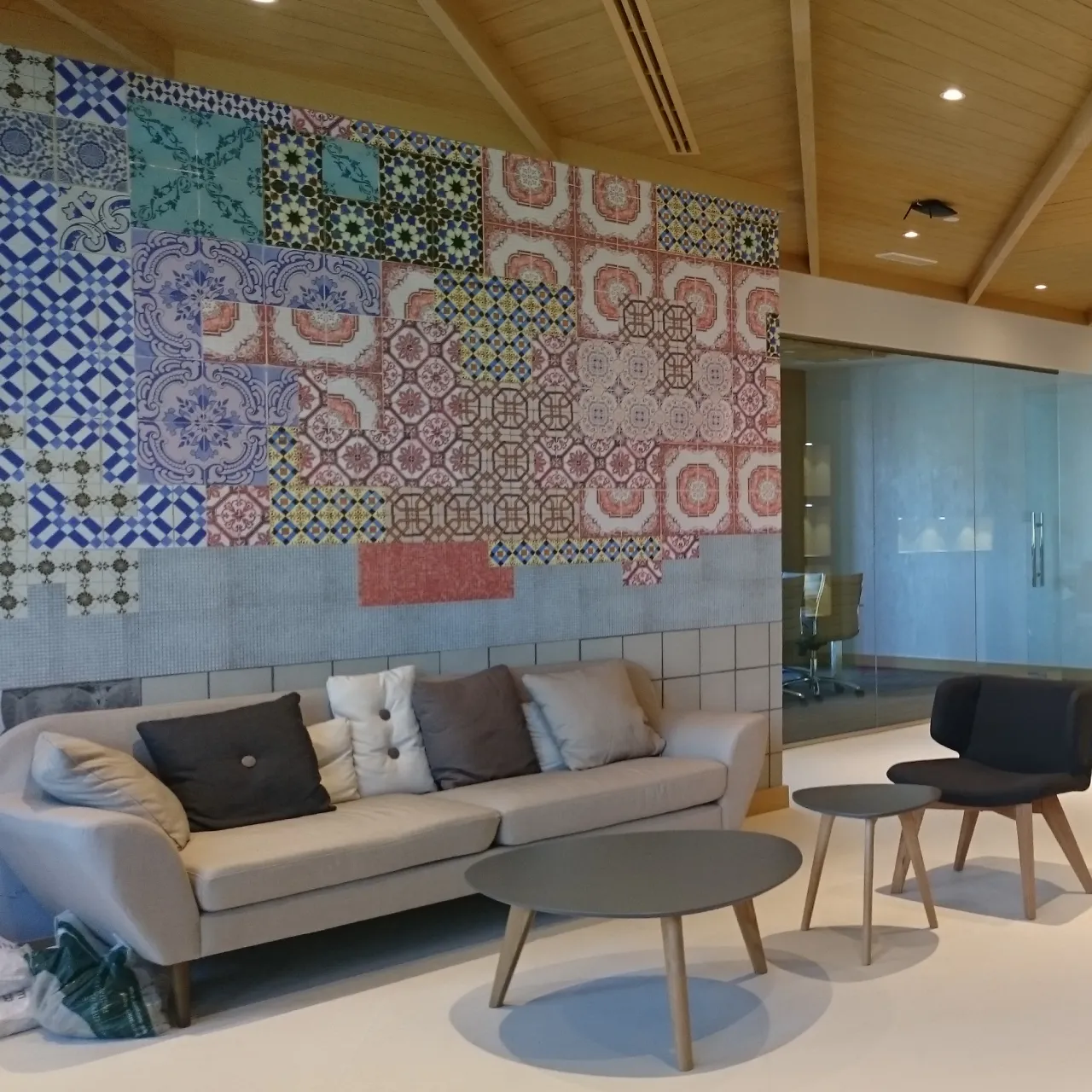 Factory office interior design in Dubai with a ceramic tile feature wall, neutral lounge seating, timber ceiling, and glass meeting room