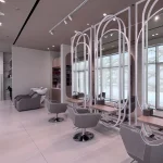 Dubai beauty salon hair styling zone with grey salon chairs, white oval mirror structures, light wood worktops, track lights, and large windows