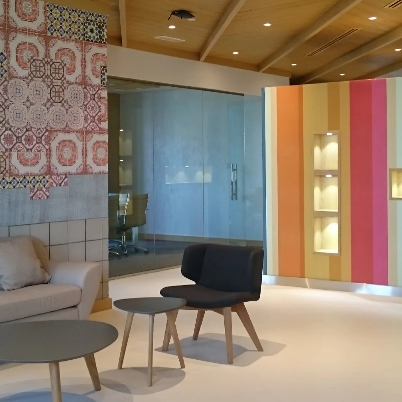 Factory office design featuring a client lounge, patterned ceramic wall, glass meeting room, colorful display partition, and timber roof