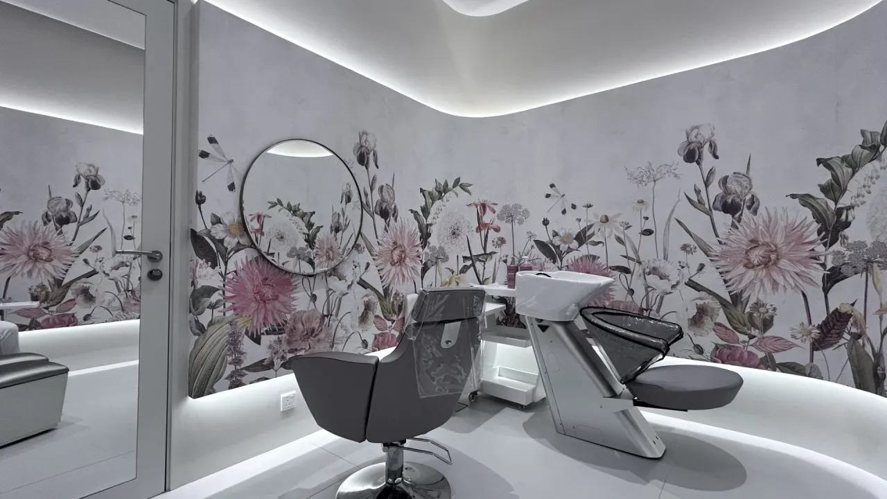 Hair washing and treatment room in a Dubai beauty salon with floral wall mural, round mirror, grey styling chair, shampoo basin, and hidden LED lighting