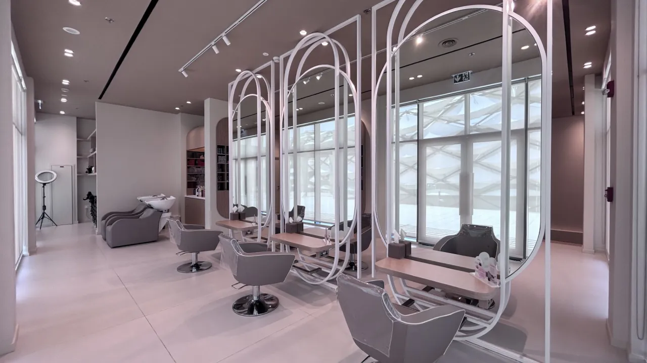 Modern Dubai beauty salon hair styling area with grey chairs, large oval mirror frames, pale worktops, track lighting, and window light