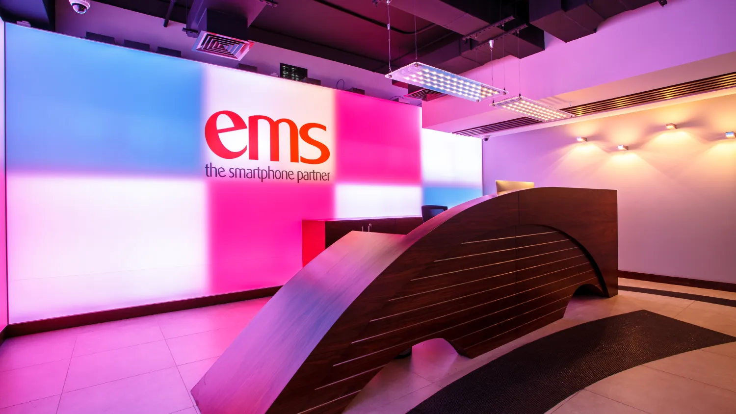 Software company interior featuring a sculptural curved reception counter, pink and blue backlighting, and an exposed black services ceiling
